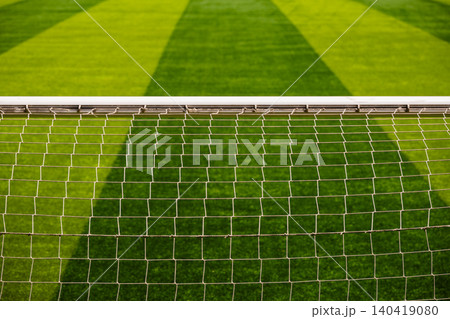 Horizontal view of a soccer goal post crossbar and white net mesh over a striped green grass pitch Horizontal view of a soccer goal post crossbar and white net mesh over a striped green grass pitch 140419080