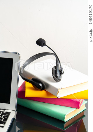 Headset rests on a stack of books near a laptop during study time Headset rests on a stack of books near a laptop during study time 140419170