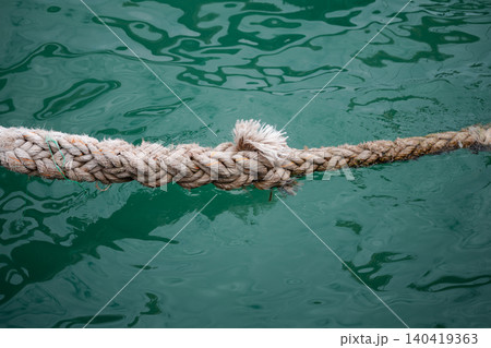 Close-up of a weathered, frayed nautical rope suspended over turquoise ocean water Close-up of a weathered, frayed nautical rope suspended over turquoise ocean water 140419363
