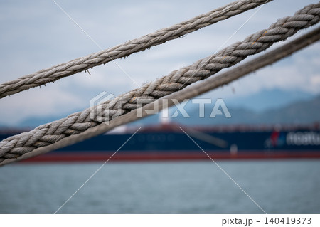 Three parallel ropes in sharp focus leading toward a blurred large blue freighter ship Three parallel ropes in sharp focus leading toward a blurred large blue freighter ship 140419373