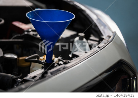 A blue funnel sits on a car engine for pouring fluids during maintenance. 140419415