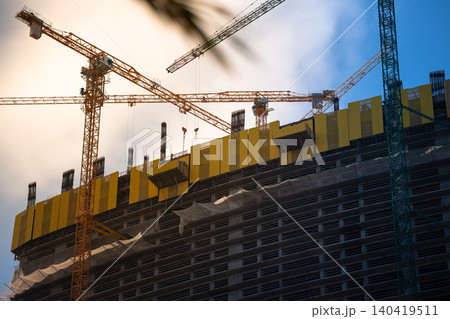 Tall skyscraper structure under construction with yellow safety scaffolding and tower cranes 140419511