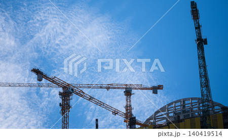 Industrial scene showing yellow and green tower cranes at a skyscraper construction site 140419514