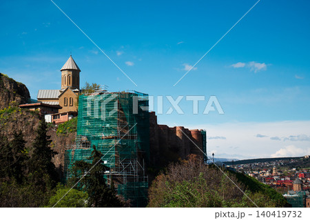 Ancient stone fortress and orthodox church under construction with scaffolding against a blue sky Ancient stone fortress and orthodox church under construction with scaffolding against a blue sky 140419732