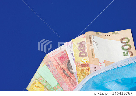 Currency from Ukraine placed under a medical mask on a blue surface Currency from Ukraine placed under a medical mask on a blue surface 140419767