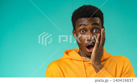 Person shows surprise while standing against a bright blue background in casual clothing 140419837