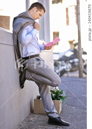 Businessman, city and unemployment with job loss or stress and thinking of career crisis. Salesman, pink slip and mental health or anxiety in street, reading and fired or termination of work contract Businessman, city and unemployment with job loss or stress and thinking of career crisis. Salesman, pink slip and mental health or anxiety in street, reading and fired or termination of work contract 140419870