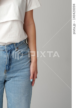 Person wearing white top and blue jeans showing hand in studio setting 140420094