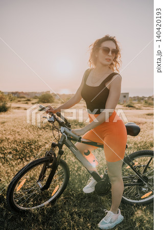 Woman bicycle summer, a young woman in sunglasses riding a mountain bike on a meadow at sunset with soft lighting and copy space Woman bicycle summer, a young woman in sunglasses riding a mountain bike on a meadow at sunset with soft lighting and copy space 140420193