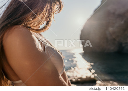 Woman bikini beach Young woman in beige swimwear relaxing on a pebble shore near cliffs during golden hour sunset 140420261