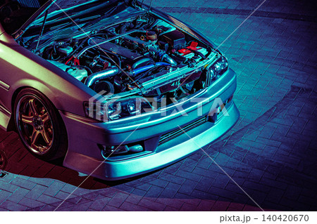 Custom car with open hood and engine exposed at night in a garage setting with bright lights Custom car with open hood and engine exposed at night in a garage setting with bright lights 140420670