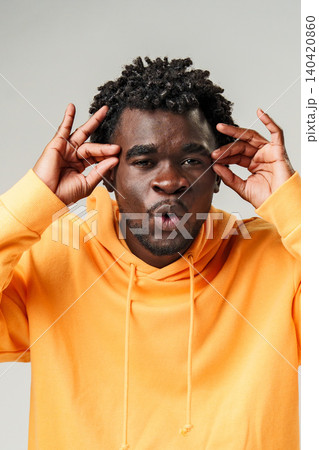 Man makes funny face while wearing orange hoodie indoors in a studio setting 140420860