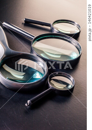Three magnifying glasses on a dark surface in different sizes showing clear glass 140421019