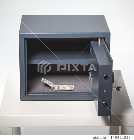 Money is placed inside a grey safe sitting on a white table in a well-lit room 140421022
