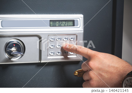 Entering a code on a silver safe with a keypad and display screen in an indoor setting Entering a code on a silver safe with a keypad and display screen in an indoor setting 140421145