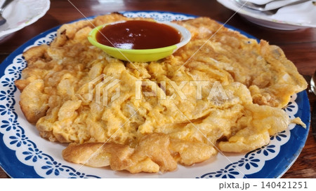 Golden Crispy Thai Omelet Served with Spicy Chili Sauce on a Blue Patterned Plate Golden Crispy Thai Omelet Served with Spicy Chili Sauce on a Blue Patterned Plate 140421251