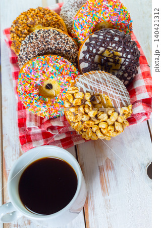 Colorful donuts and coffee on a table with a checkered cloth in the morning sunlight Colorful donuts and coffee on a table with a checkered cloth in the morning sunlight 140421312