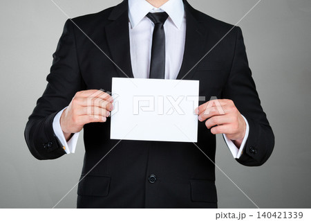 Businessman holds blank paper against gray background in office setting during daytime 140421339