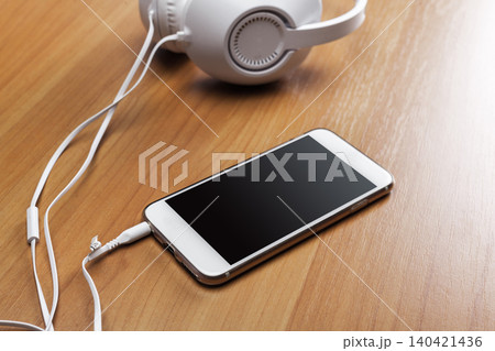 Mobile phone and headphones are placed on a wooden table in a quiet room 140421436