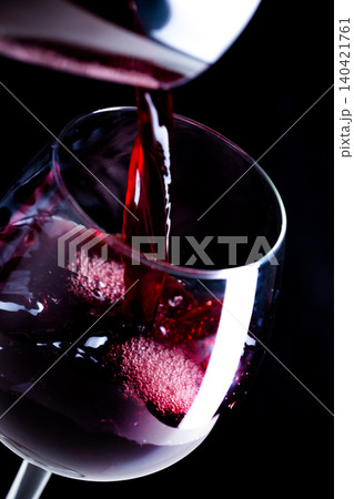 Pouring red wine into a clear glass near a dark background Pouring red wine into a clear glass near a dark background 140421761