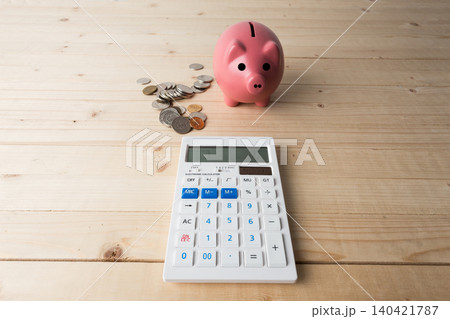Saving money with a piggy bank and a calculator on a wooden table in a simple setup Saving money with a piggy bank and a calculator on a wooden table in a simple setup 140421787