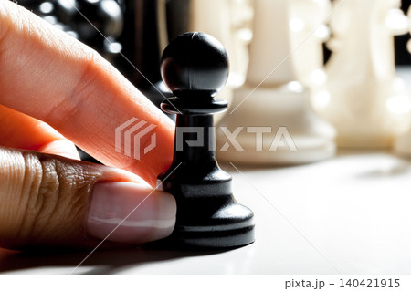 Hand holds black chess pawn with white pieces in background during a game of chess Hand holds black chess pawn with white pieces in background during a game of chess 140421915