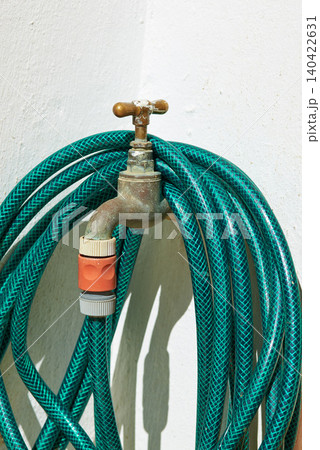 Tap, pipe and garden hose with attachment for water, pressure or environmental care at home. Closeup of faucet with plastic hosepipe rolled up on wall for liquid supply, service or outdoor gardening Tap, pipe and garden hose with attachment for water, pressure or environmental care at home. Closeup of faucet with plastic hosepipe rolled up on wall for liquid supply, service or outdoor gardening 140422631
