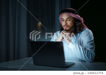 Man in white clothes uses laptop at night in a lit room with curtains Man in white clothes uses laptop at night in a lit room with curtains 140422754