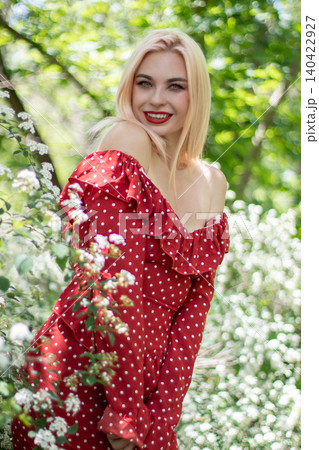Smiling Blonde Woman in Red Dress Near Blossoms Smiling Blonde Woman in Red Dress Near Blossoms 140422927