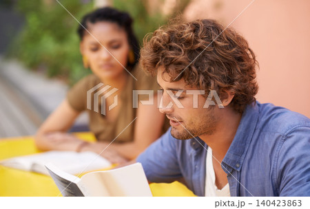Face, education and student man reading on college or university campus for learning and study. Book, scholarship and pupil with young person outdoor for research on break or recess at school 140423863