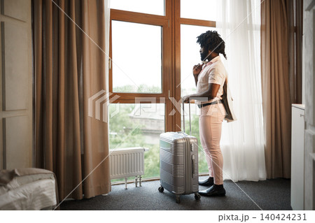 Portrait of a black man businessman with packed suitcase near large window in hotel room Portrait of a black man businessman with packed suitcase near large window in hotel room 140424231