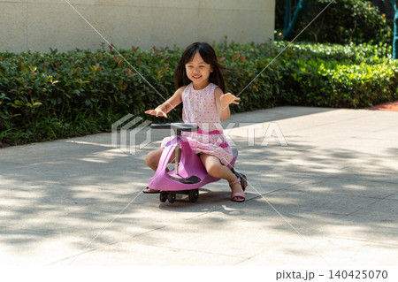 Cute Asian Little Girl Riding Wiggle Car Outdoors in Sunny Park 140425070