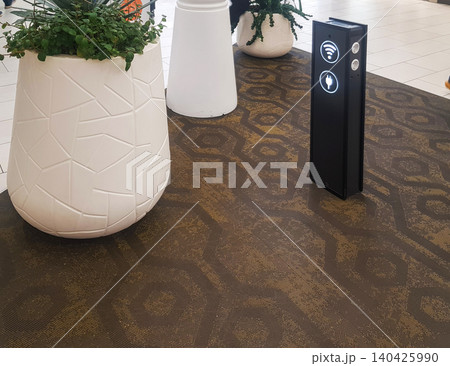 Wi-Fi zone with a rack for charging gadgets via usb and at the airport or supermarket, nearby plants in white flower pots Wi-Fi zone with a rack for charging gadgets via usb and at the airport or supermarket, nearby plants in white flower pots 140425990