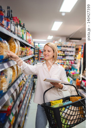 Woman shopping for groceries in supermarket aisle with basket Woman shopping for groceries in supermarket aisle with basket 140427399