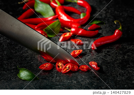 Kitchen knife and slices of red hot chili peppers on a kitchen table. Kitchen knife and slices of red hot chili peppers on a kitchen table. 140427829