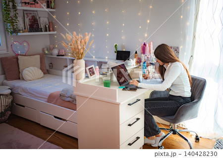 Teenager girl studying on laptop at desk in cozy bedroom Teenager girl studying on laptop at desk in cozy bedroom 140428230