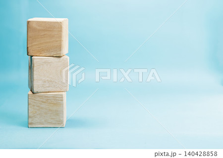 A vertical tower of three blank wooden cubes stacked on the left side over a solid light blue background, creating a clean template for concepts or words. High Quality Photo 140428858