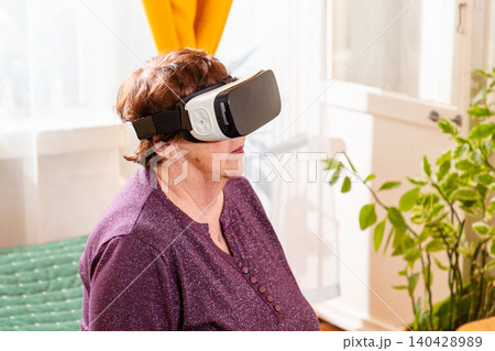 Elderly user experiencing virtual reality simulation with VR headset in a comfortable home setting. Digital inclusion and innovation concept. Aging with technology and curiosity. Close up Elderly user experiencing virtual reality simulation with VR headset in a comfortable home setting. Digital inclusion and innovation concept. Aging with technology and curiosity. Close up 140428989