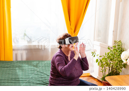 Elderly woman testing virtual reality headset and exploring digital world indoors. Smart technology and future living concept. Active retirement and innovation engagement. Elderly woman testing virtual reality headset and exploring digital world indoors. Smart technology and future living concept. Active retirement and innovation engagement. 140428990