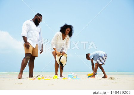 Happy Black family building sandcastle together on beach 140429203
