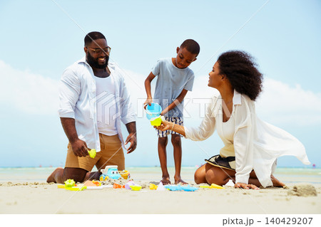 Happy Black family building sandcastle together on beach Happy Black family building sandcastle together on beach 140429207