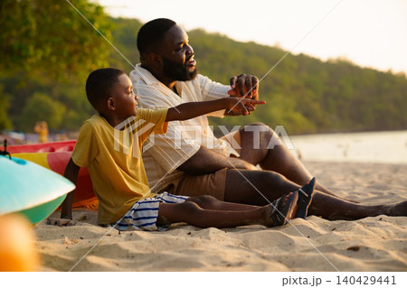 African American father and son watching sunset on the beach 140429441