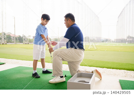 Young boy practicing golf swing with professinoal golf instructor at driving range 140429505