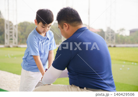 Young boy practicing golf swing with professinoal golf instructor at driving range 140429506