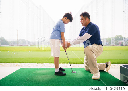 Young boy practicing golf swing with professinoal golf instructor at driving range 140429510