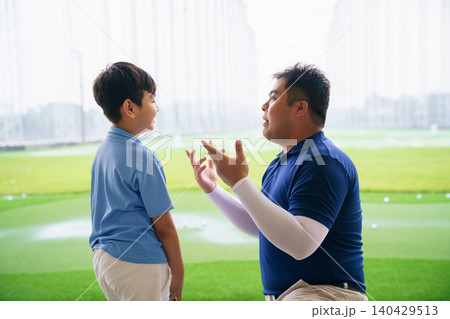 Young boy practicing golf swing with professinoal golf instructor at driving range 140429513