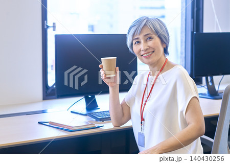 オフィスのデスクで紙コップを持って微笑むグレーヘア女性 オフィスのデスクで紙コップを持って微笑むグレーヘア女性 140430256