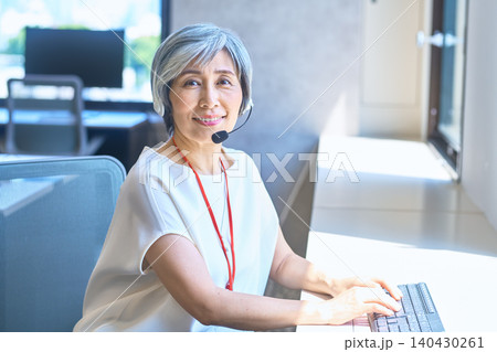 ヘッドセットを着けてキーボードを操作するグレーヘア女性 ヘッドセットを着けてキーボードを操作するグレーヘア女性 140430261