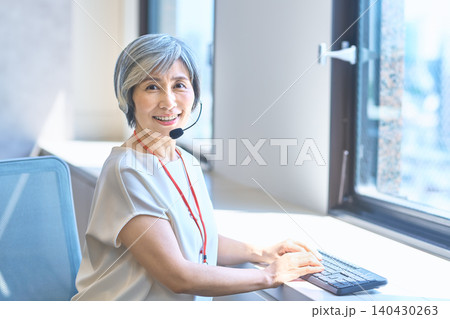ヘッドセットで対応しながら笑顔で仕事するグレーヘア女性 ヘッドセットで対応しながら笑顔で仕事するグレーヘア女性 140430263