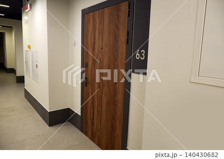 Modern wooden apartment or hotel room door numbered 63 in a clean indoor corridor. 140430682